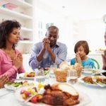 Family around dinner table offering Thanksgiving prayers