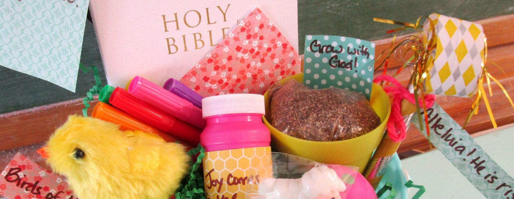 Light blue bucket filled with green paper grass and numerous items, including (from left, clockwise) a stuffed chick, assorted markers, a Bible, a plastic pot with dirt, a party noisemaker, a sheep figurine, a bottle of bubbles, and an egg