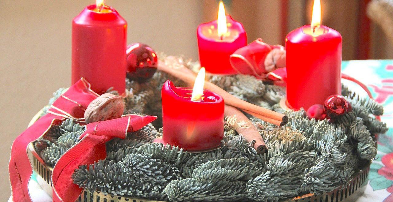 Four lit red pillar candles among evergreen branches, red ribbon, and a red ornament