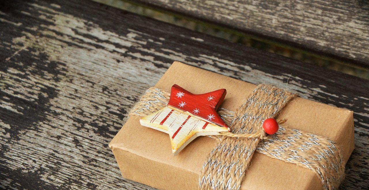 Box wrapped in brown paper and ribbon and topped with a red and white star on a weathered wooden background