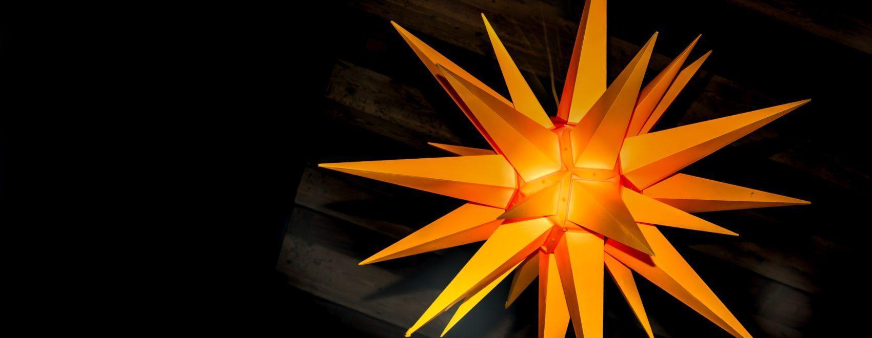 Close-up of orange many-pointed three-dimensional star in front of a black background
