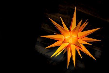 Close-up of orange many-pointed three-dimensional star in front of a black background