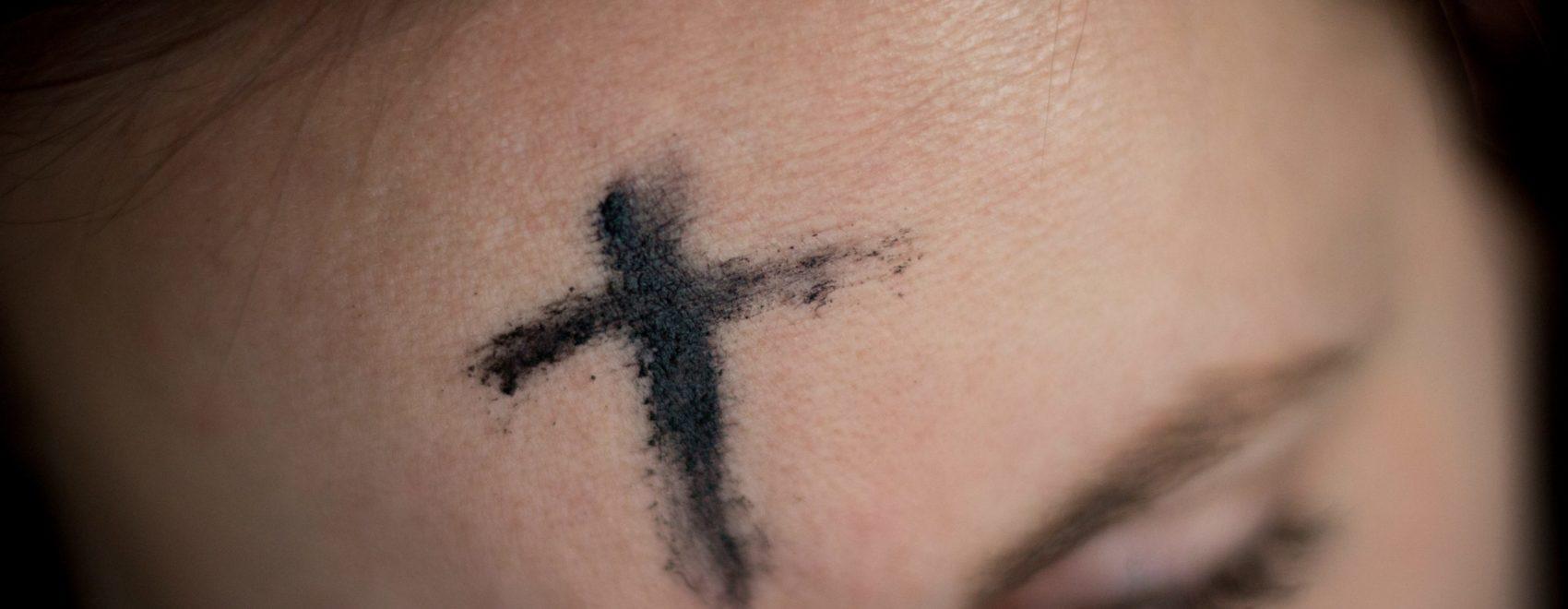Close-up of ashes in the shape of a cross on the forehead of a person with light skin tone