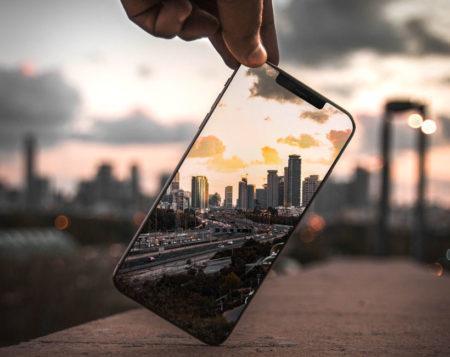 Person holding phone which is showing city-scape with city also visible in background.