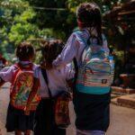 Backs of three children walking together wearing backpacks.