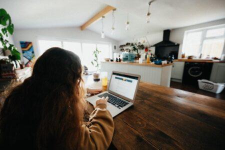 Girl with brown hair working on laptop at kitchen table.