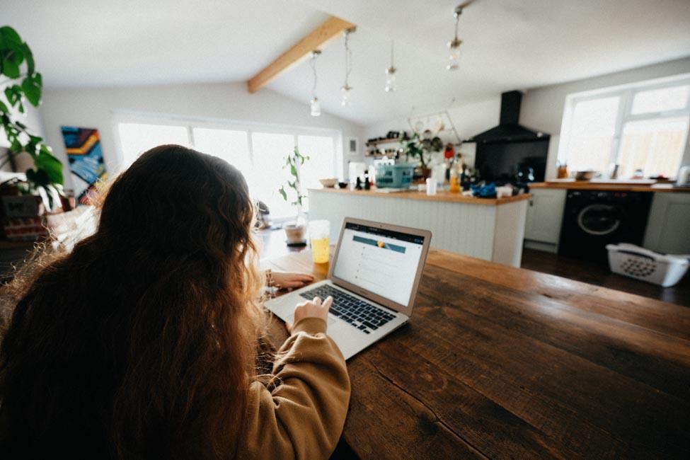 Girl with brown hair working on laptop at kitchen table.