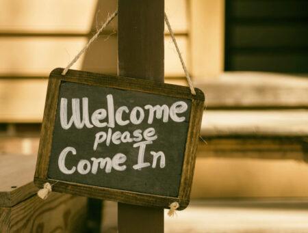 Small chalkboard hanging from twine with white words, "Welcome please come in."