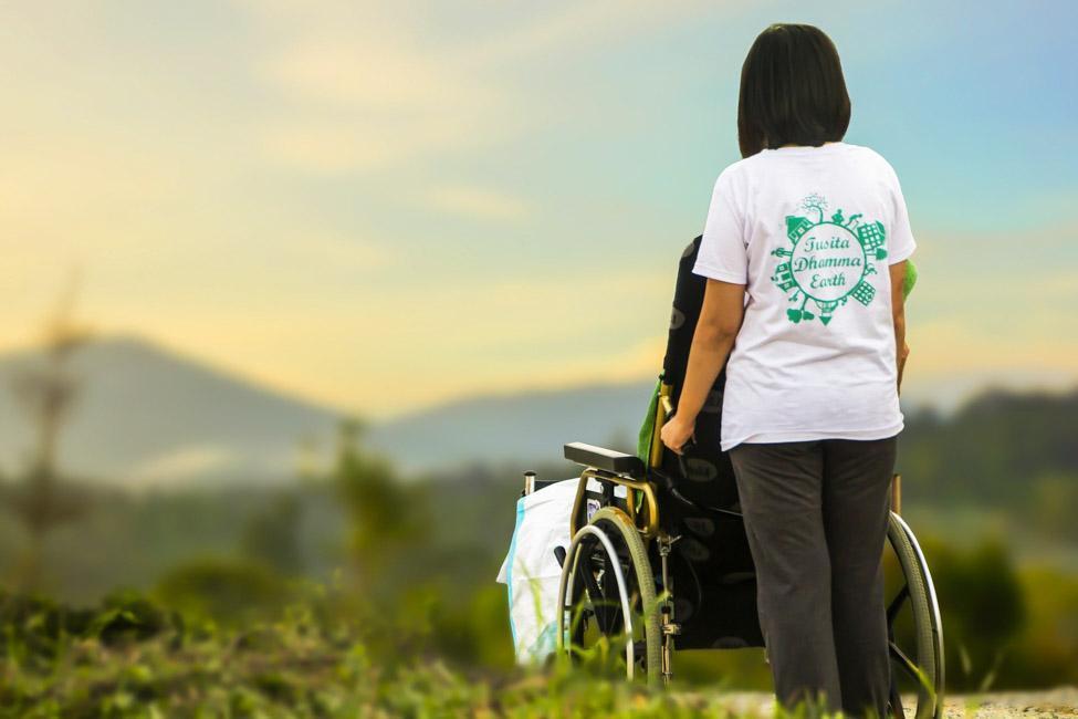 Woman in white shirt pushing wheelchair with mountain range in background.
