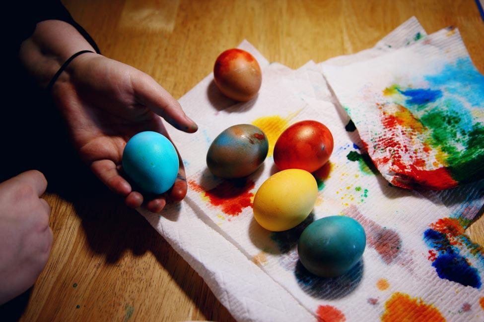 Egged dyed different colors on a paper towel stained with dye. One light blue egg is held in a hand.