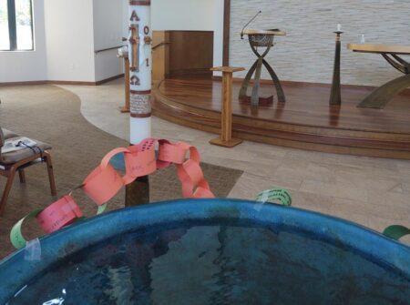 A large font of water with a paper chain and paschal candle in the background.