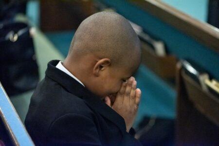 Young boy sitting in pew with hands folded in prayer.