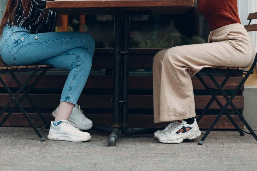 The bottom view of two woman legs sitting at table in street cafe.