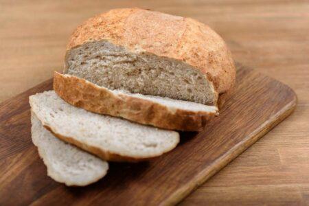 A loaf of brown bread with three slices cut on a wooden board.