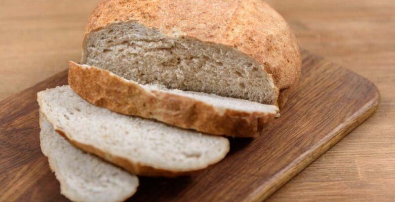 A loaf of brown bread with three slices cut on a wooden board.