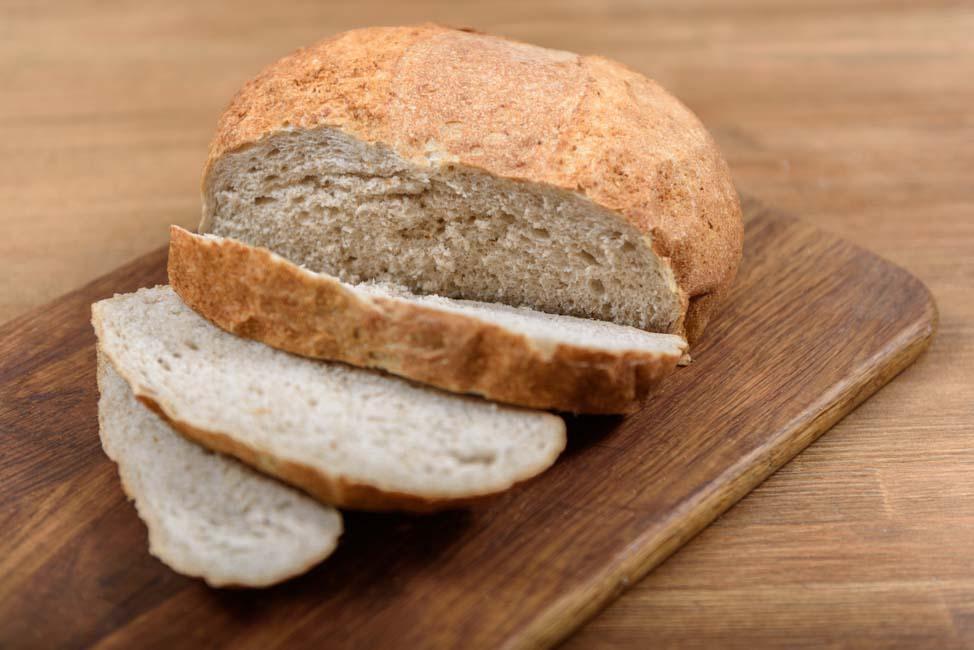 A loaf of brown bread with three slices cut on a wooden board.