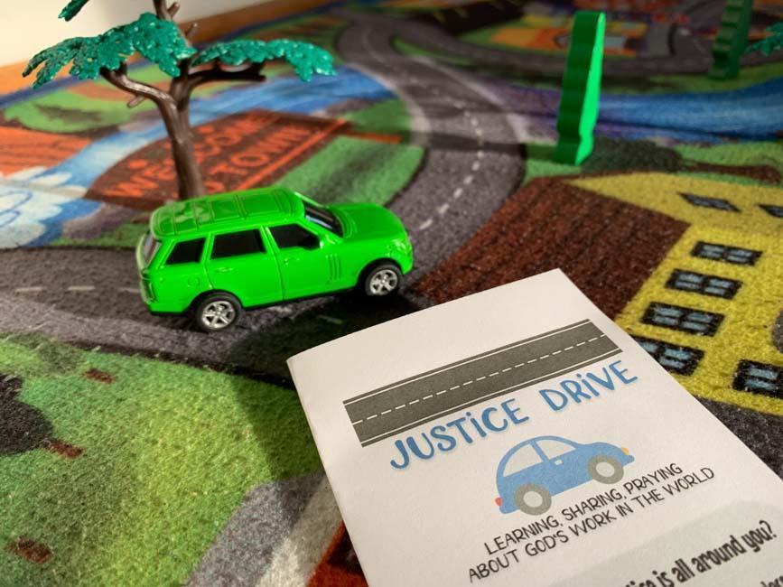 Toy green car on map rug with justice drive handout.