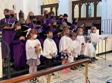 Children in choir robes holding stuffed animals.