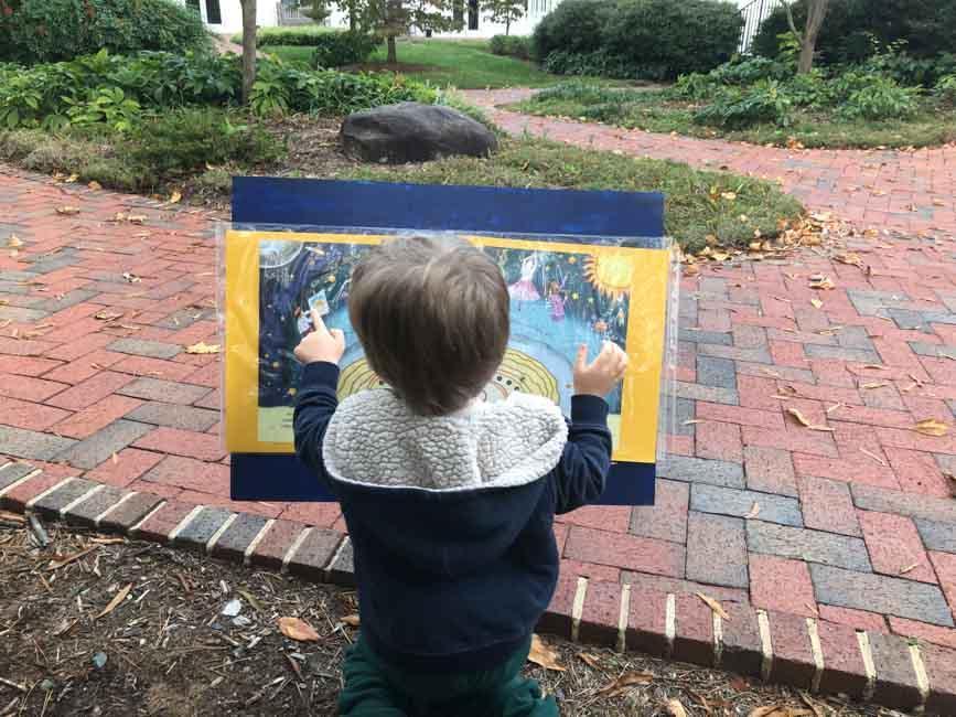 Young child with brown hair looks at pages of a storybook attached to a blue sign.