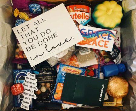 A cardboard box filled with treats and a note on top that reads, "let all that you do be done in love."
