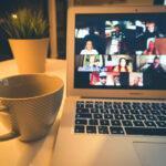Coffee cup next to computer screen with people in online meeting.