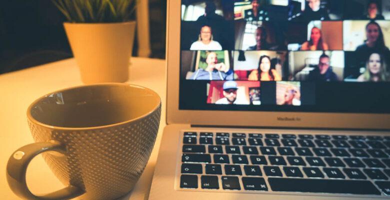 Coffee cup next to computer screen with people in online meeting.