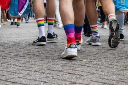 Legs and feet of people walking wearing tennis shoes and rainbow socks.
