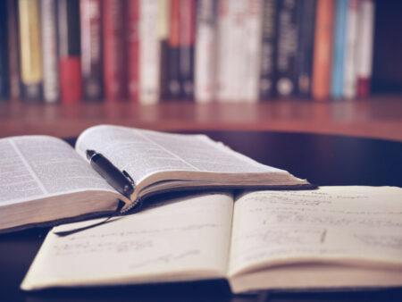 Two books open on a table with bookshelf in background.