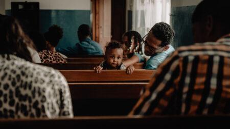 People sitting in church pews with a small child turned towards back of church looking at camera.