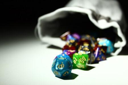 Multi-colored dice spilling out of a grey bag.