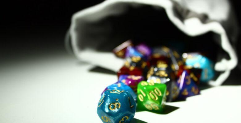 Multi-colored dice spilling out of a grey bag.