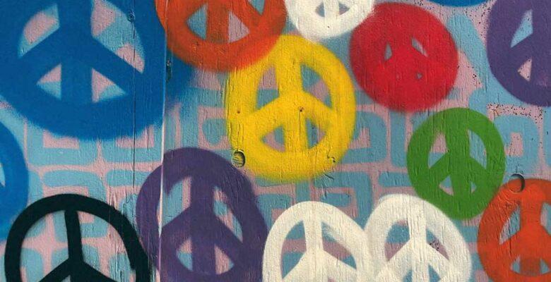 Many peace symbols of different color in spray paint on concrete wall.