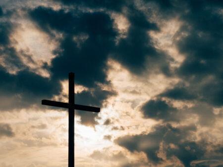 A wooden cross with blue sky and clouds in background.
