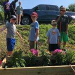 Children standing in front of wooden planted with pink flowers.
