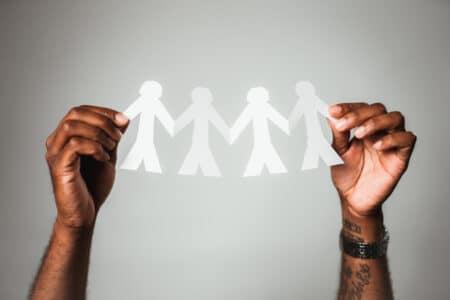 White chain of paper dolls held by hands with dark skin.