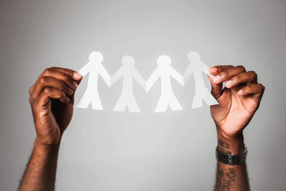 White chain of paper dolls held by hands with dark skin.