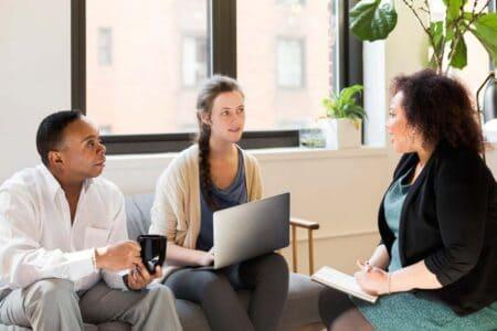 Three people sitting in chairs sharing ideas in a meeting.