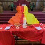Table covered in red cloth with candle and additional orange, yellow, and red cloth.