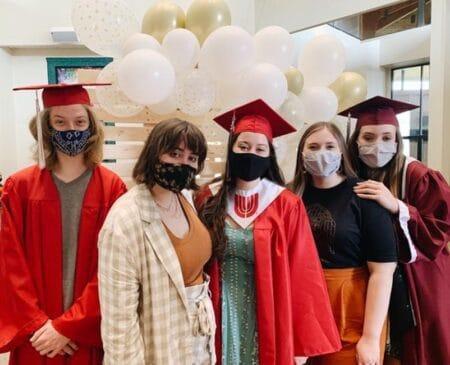 Youth with graduation caps in front of balloons.