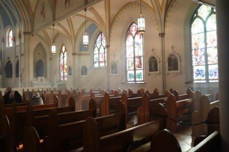 Inside of church with empty pews and light streaming in through stained glass windows.
