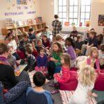 Woman sitting in chair with book surrounded by children.
