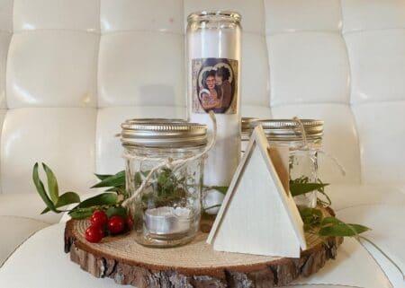 A slice of wood with large candle, jars, and greens decorating it.