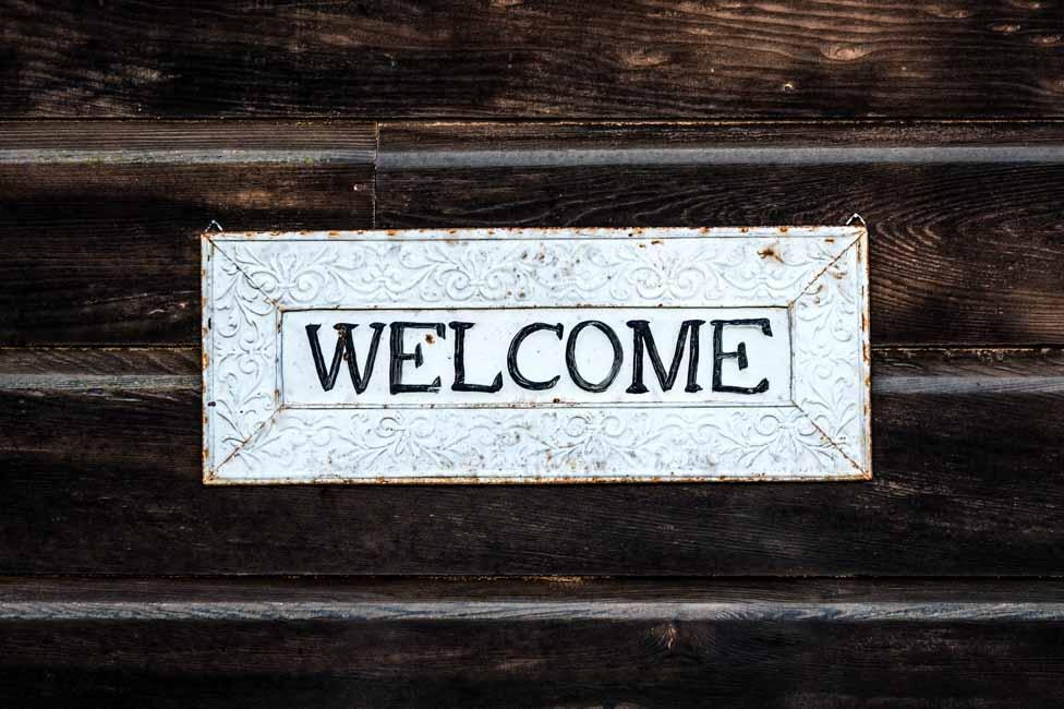 A white sign that reads "Welcome" with dark wood in the background.
