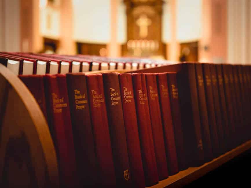 Many copies of red Book of Common Prayer on a shelf.