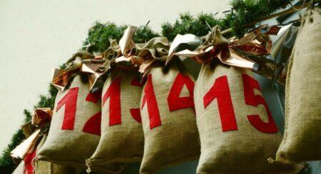Cloth bags numbered "12," "13," "14," "15" hanging below evergreen branches and gold ribbon