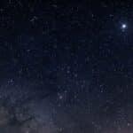 A star-filled sky with the glow from the sun on the horizon