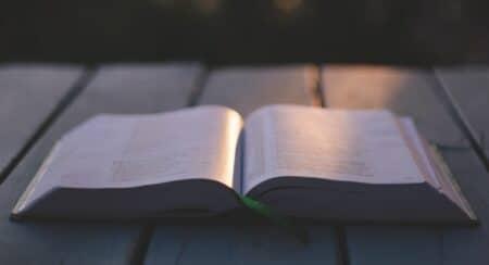 Open Bible lying flat on a gray slatted surface with a ray of light shining on the center of the Bible