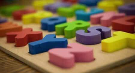 Close-up of wooden three-dimensional English alphabet puzzle with letters in yellow, purple, green, blue, red, and pink in rows on a light brown base