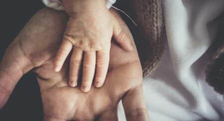 Close-up of an infant's right hand with medium light skin tone in the right palm of an older person with medium skin tone