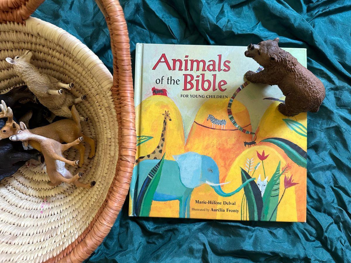 Front cover of the book "Animals of the Bible for Young Children" with several animal figurines in a basket and one figurine on top of the book